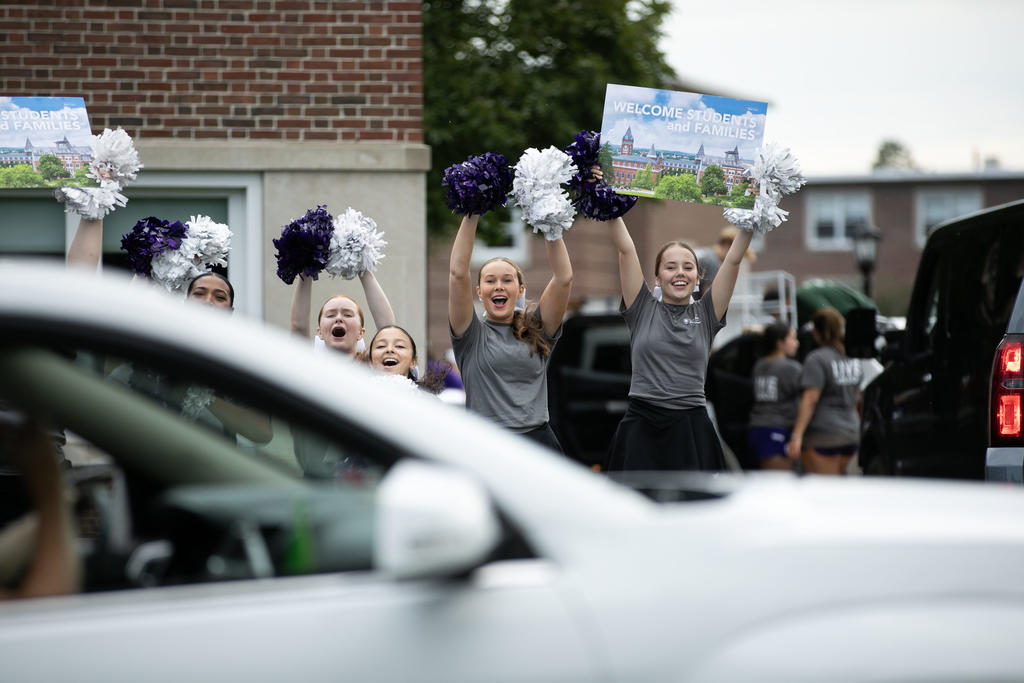 A cheer team screams out support to a car arriving on campus 
