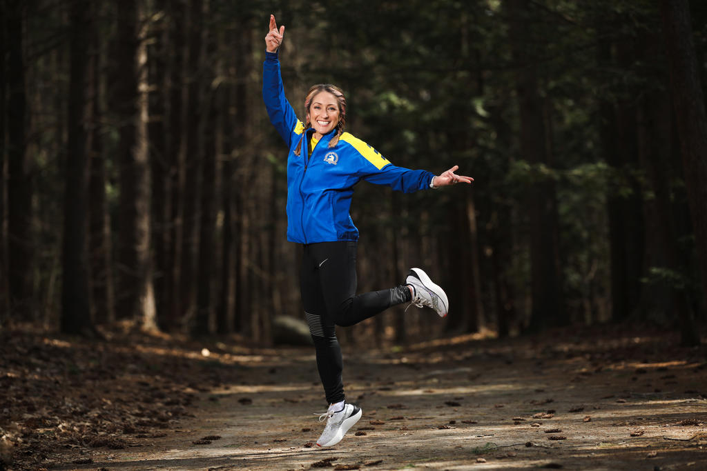 A woman runner leaps in the air and smiles on a wooded trail