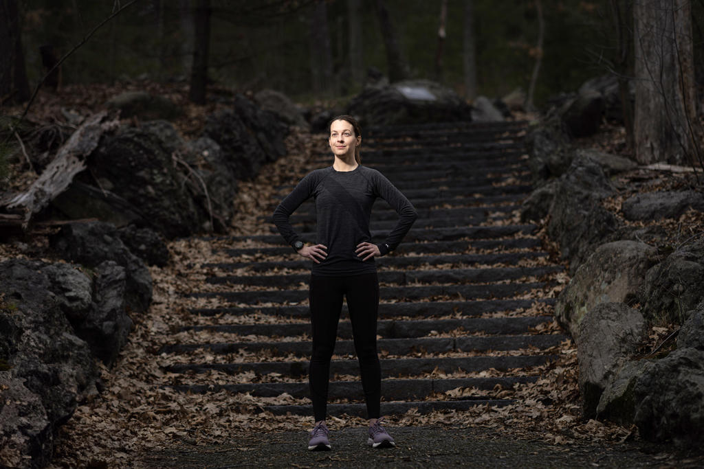 A female runner stands with hands on hips on bottom of outdoor stone staircase 