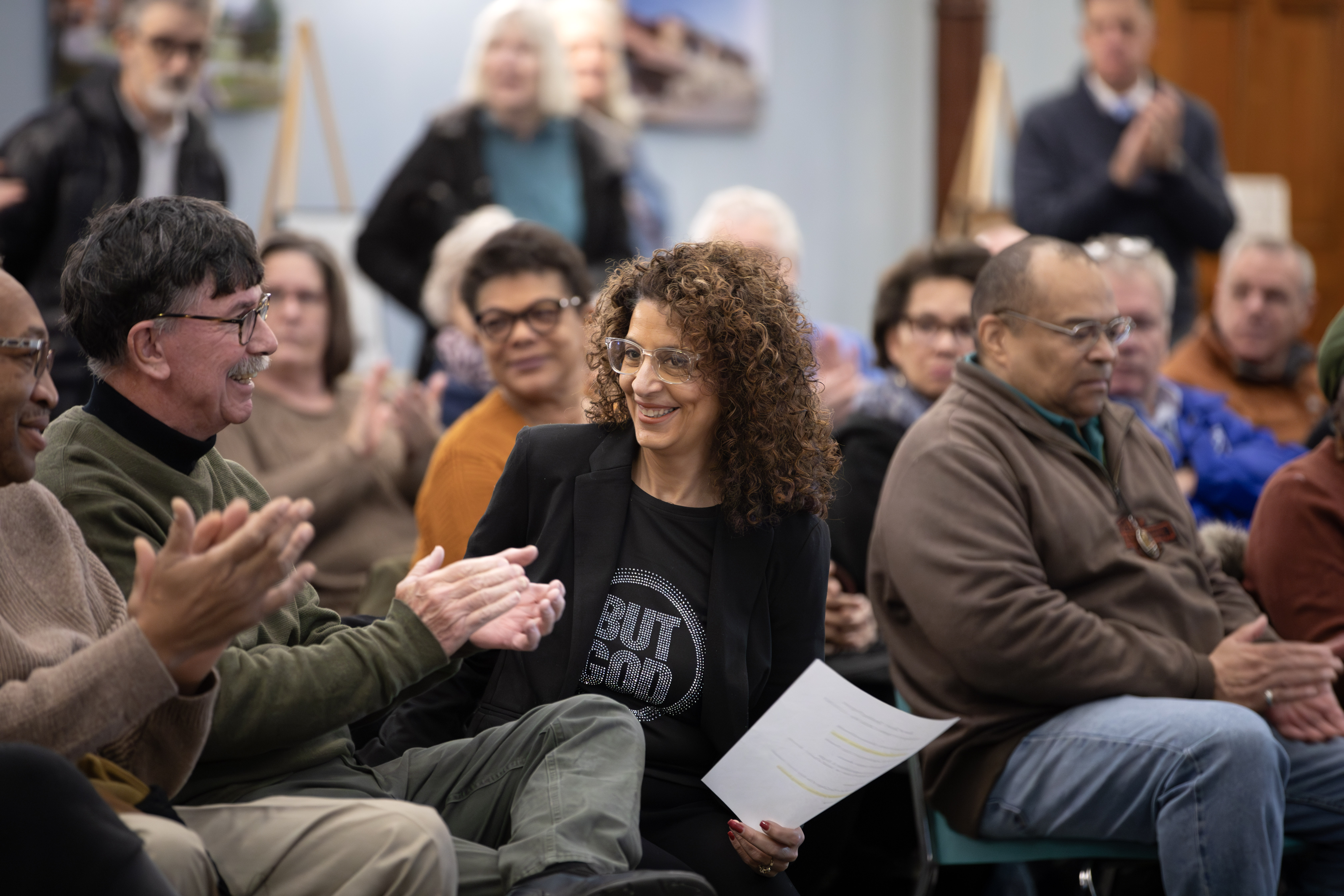 A woman is in the center of the picture with a group of people around her applauding.