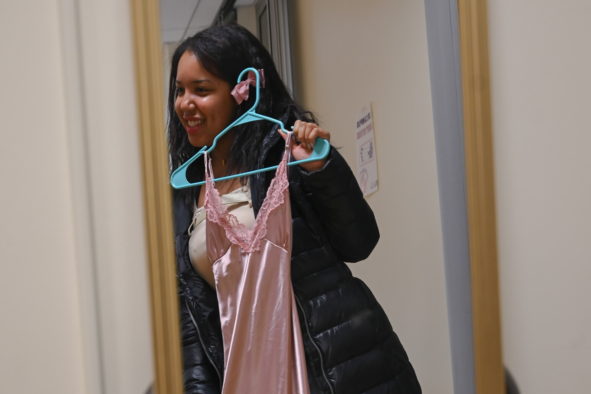 A young woman holds up a dress in front of a mirror.