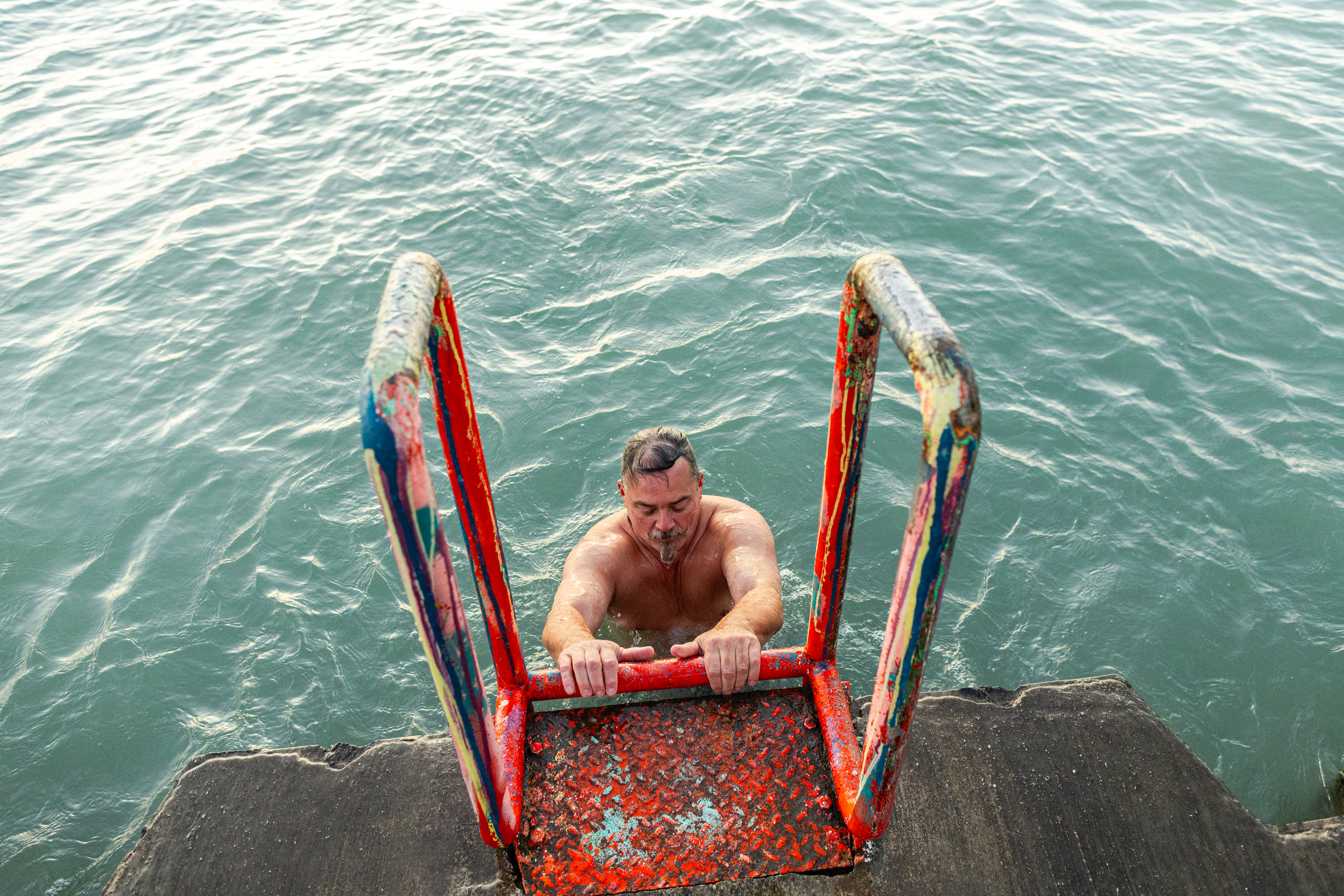 Man climbs ladder out of lake to dock