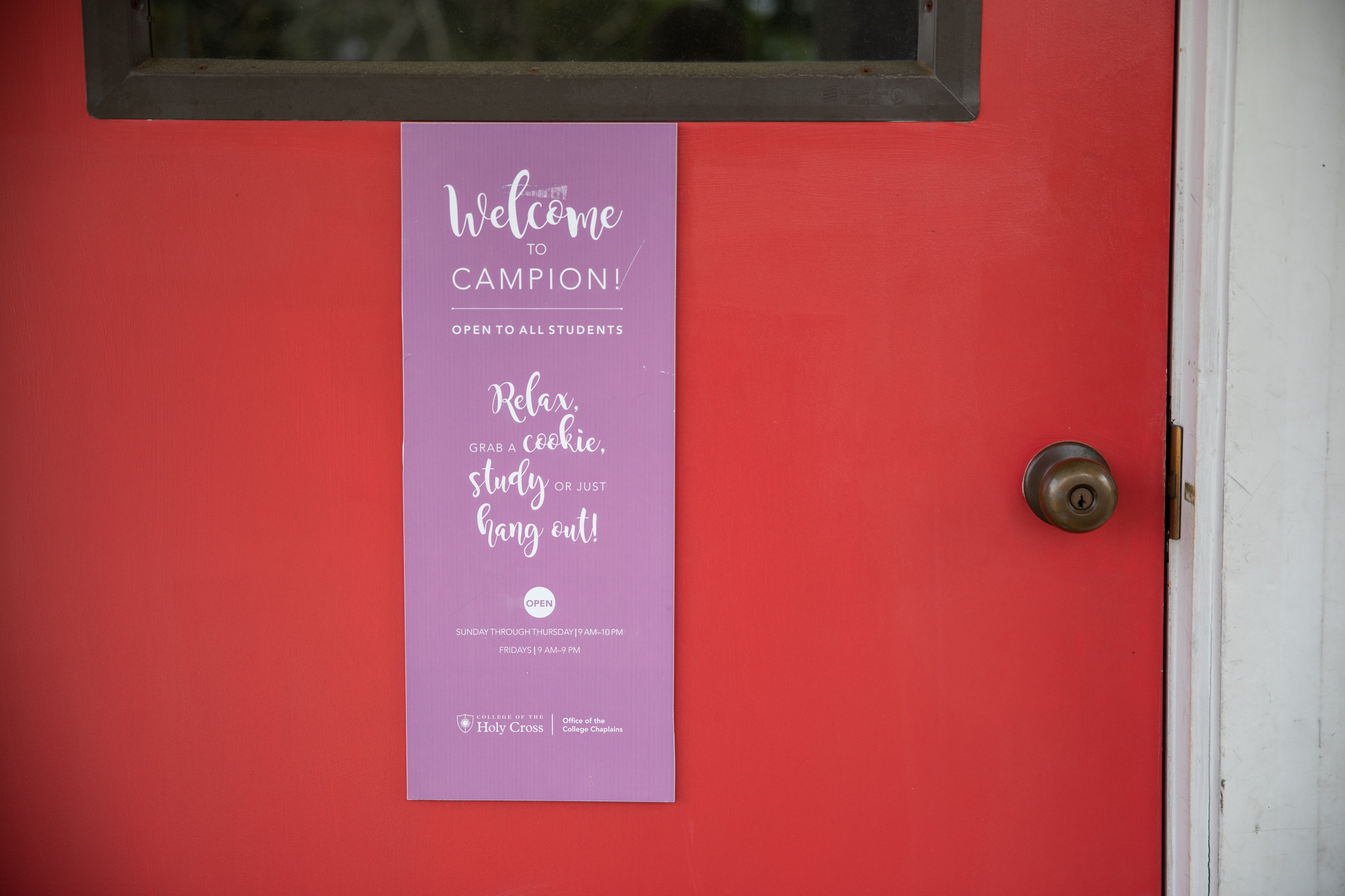 A red front door door sporting a purpler vertical sign.
