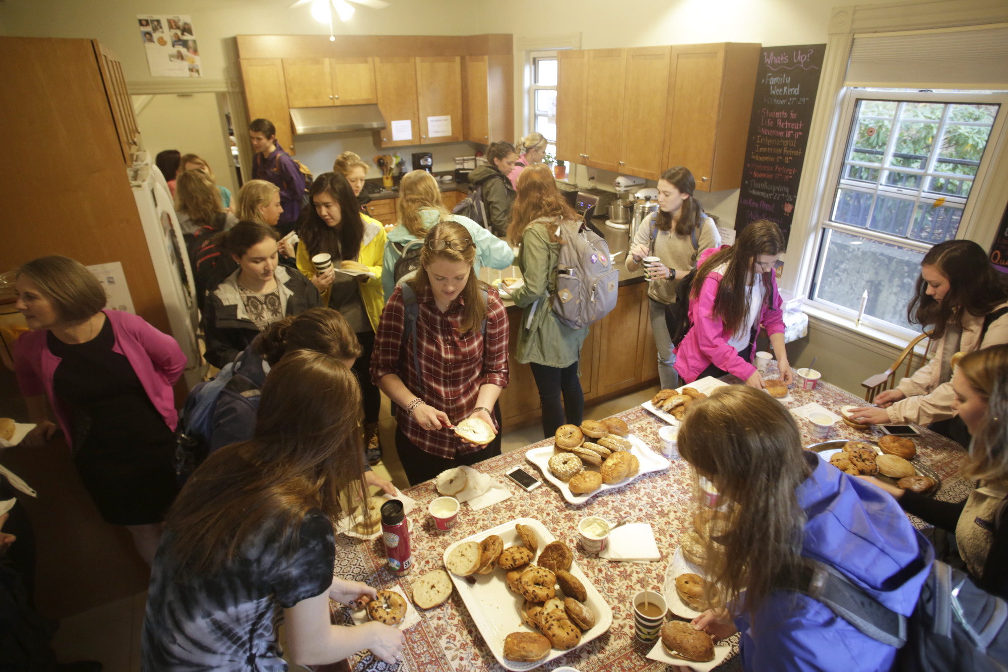 A group of people stand in a kitchen eating bagels
