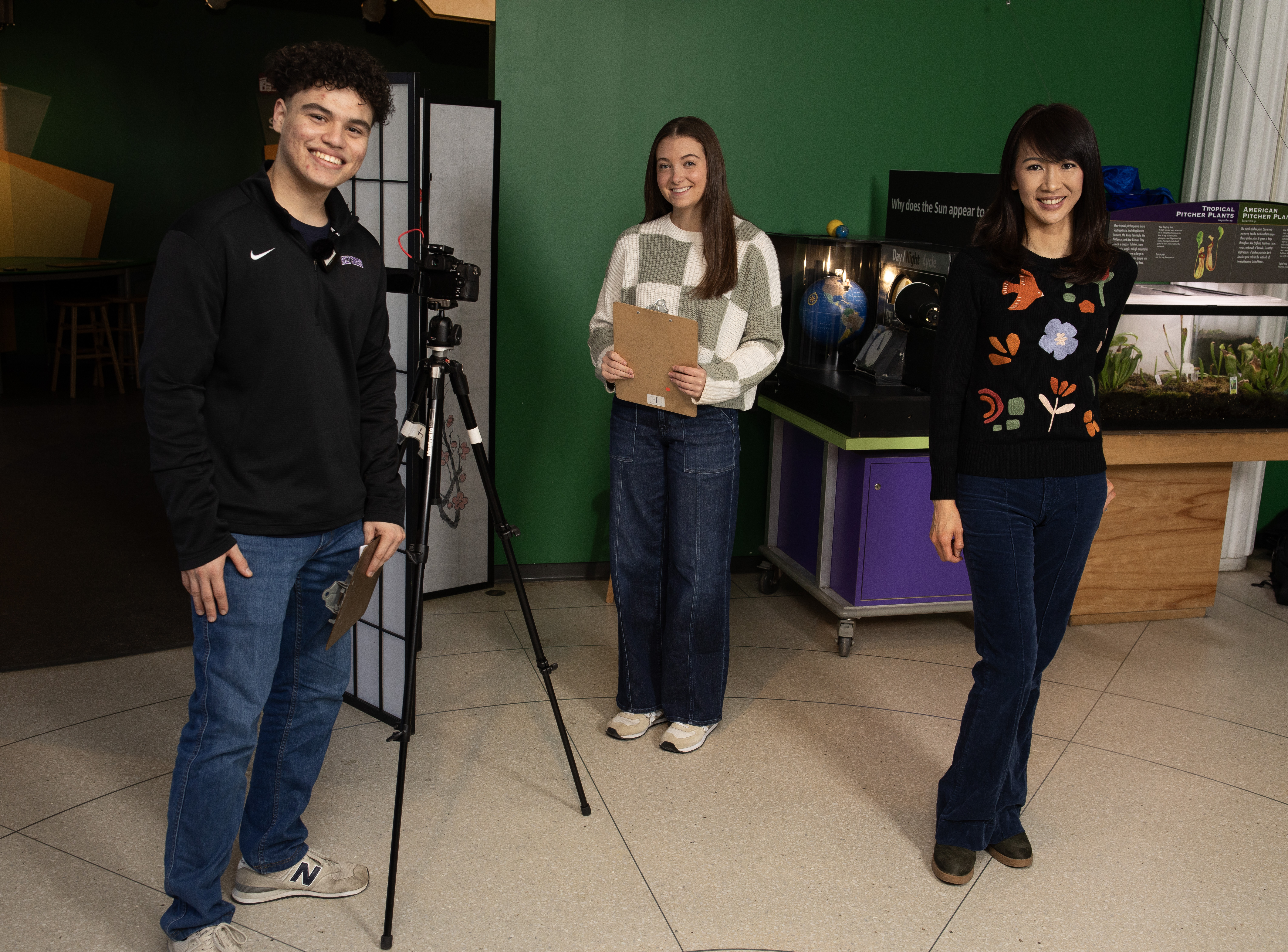Two women and one man stand near a camera tripod in the middle of a science museum.