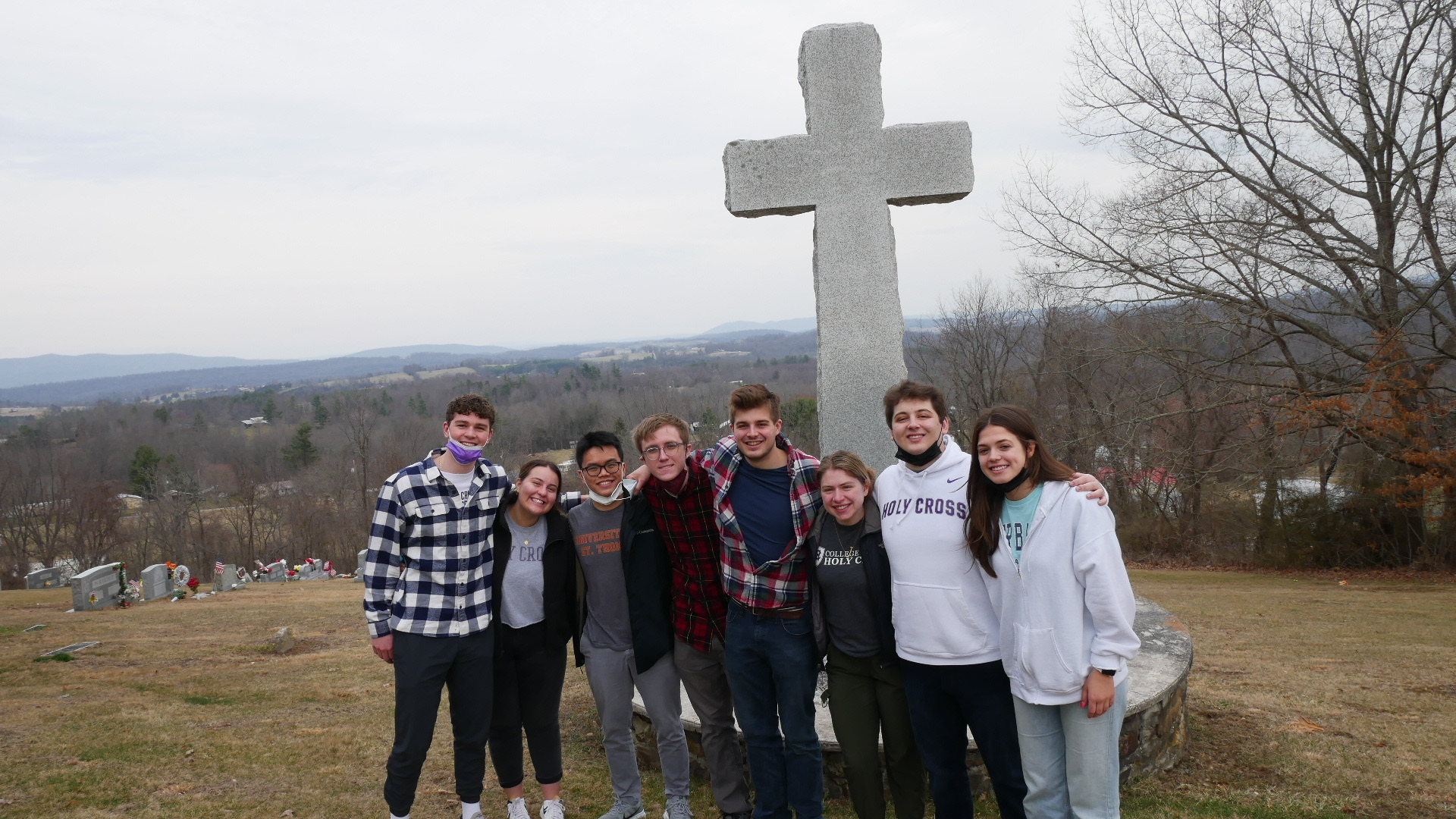 A group of young people stand by a large concrete cross
