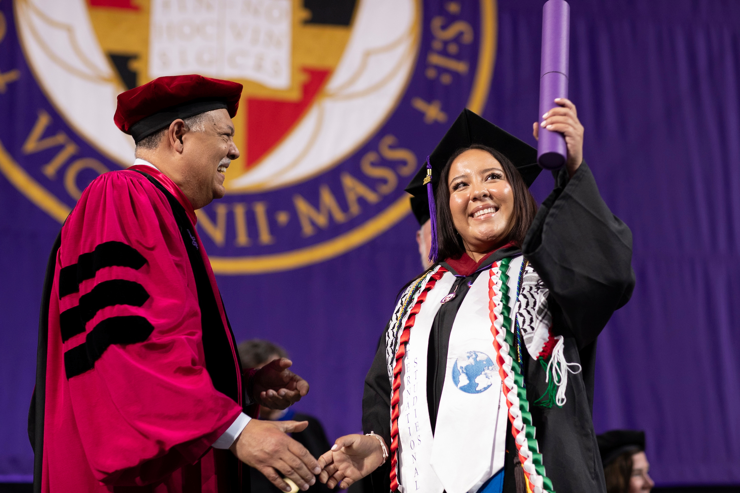Student shakes hand with college president as she receives her diploma during commencement ceremony.