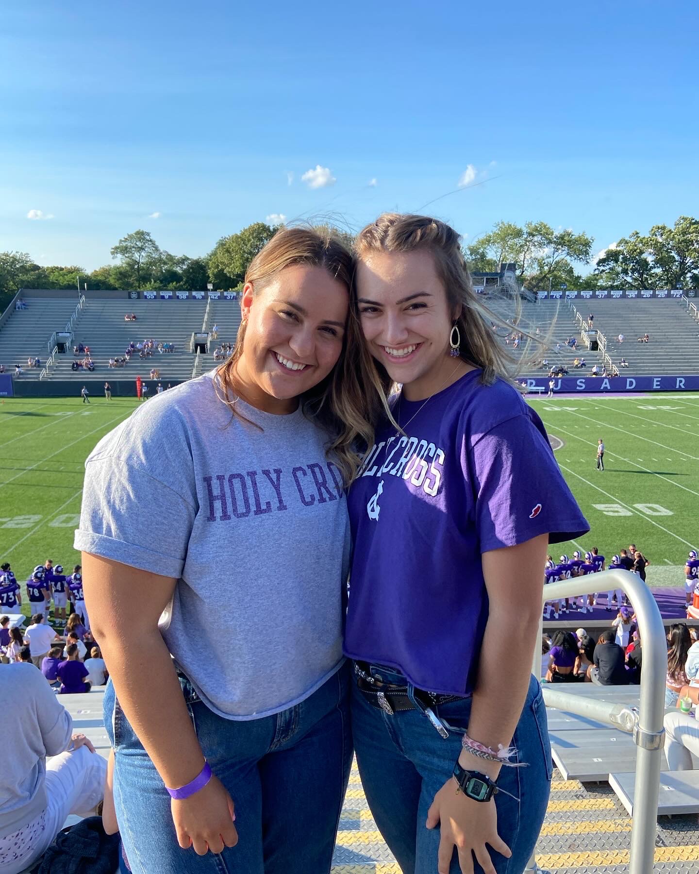 Two young woman, smiling and standing in front of a football field