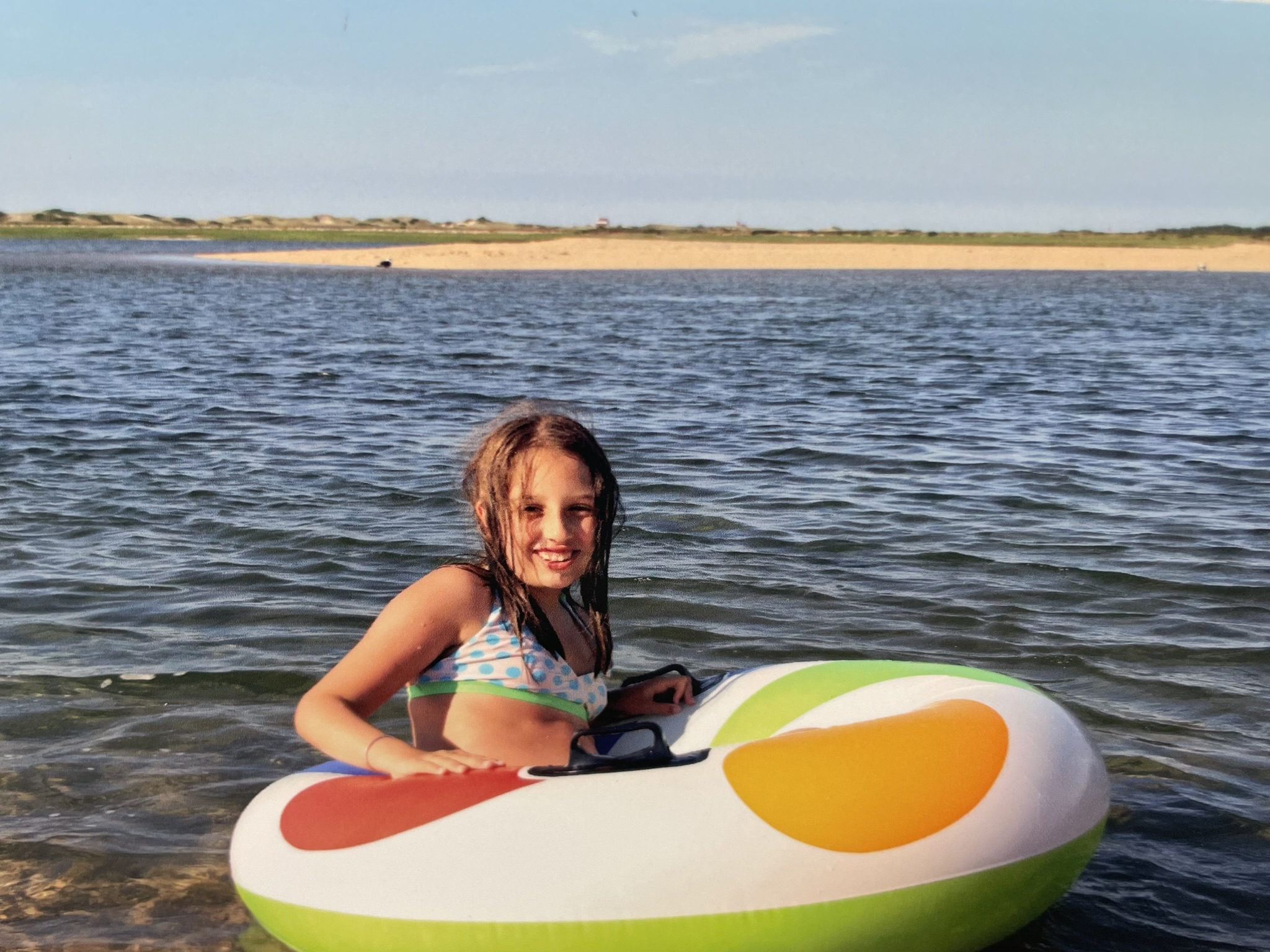 Young girl floating in a multi-colored inner tube in the ocean.