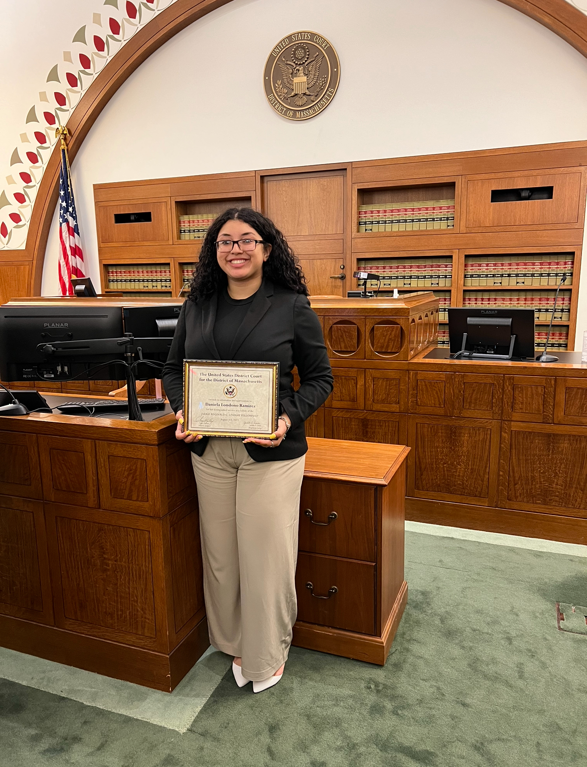 A young woman standing in a courtroom holding a framed certificate