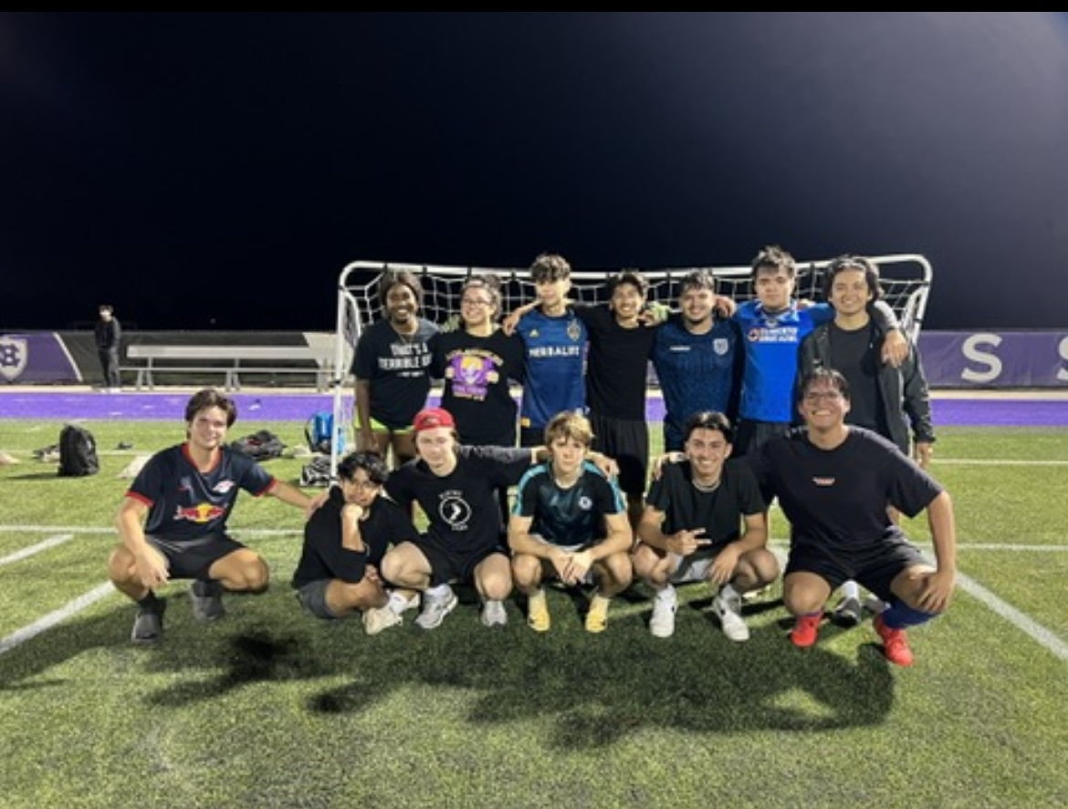A group of soccer players pose for a photo in front of a soccer net in their black uniforms