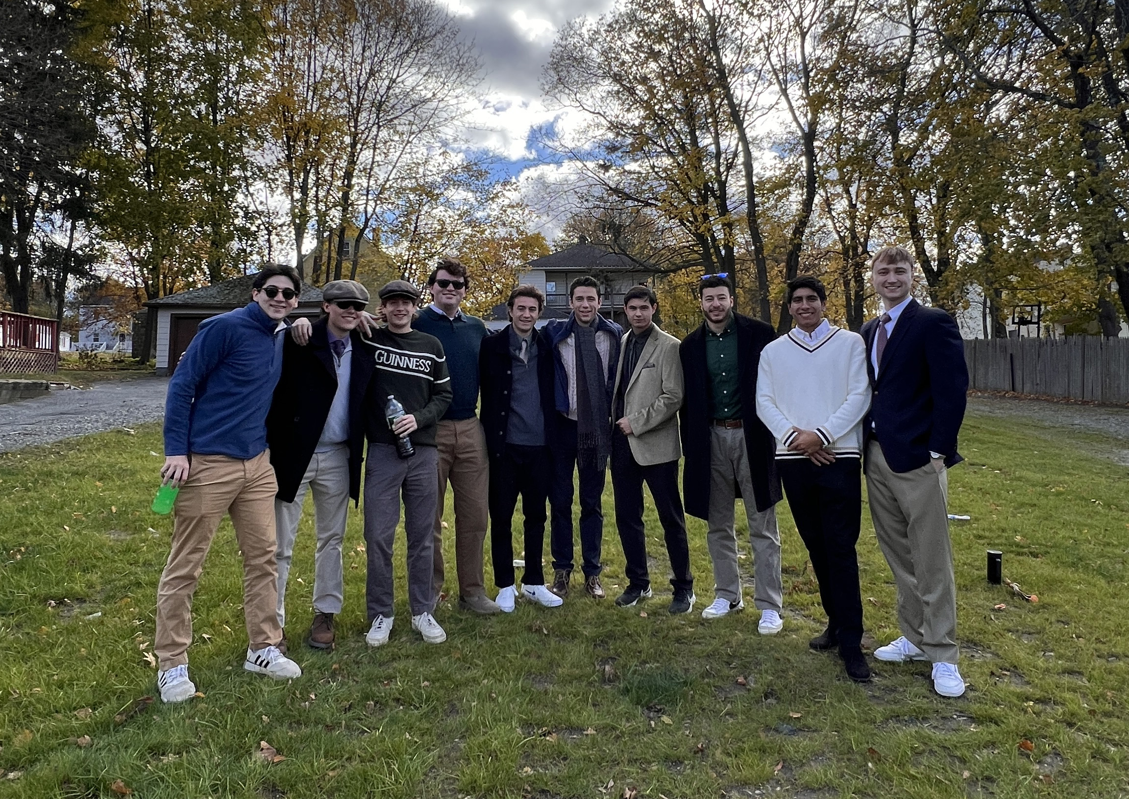 A group of young men pose for a photo in a yard with a road and fence in the background