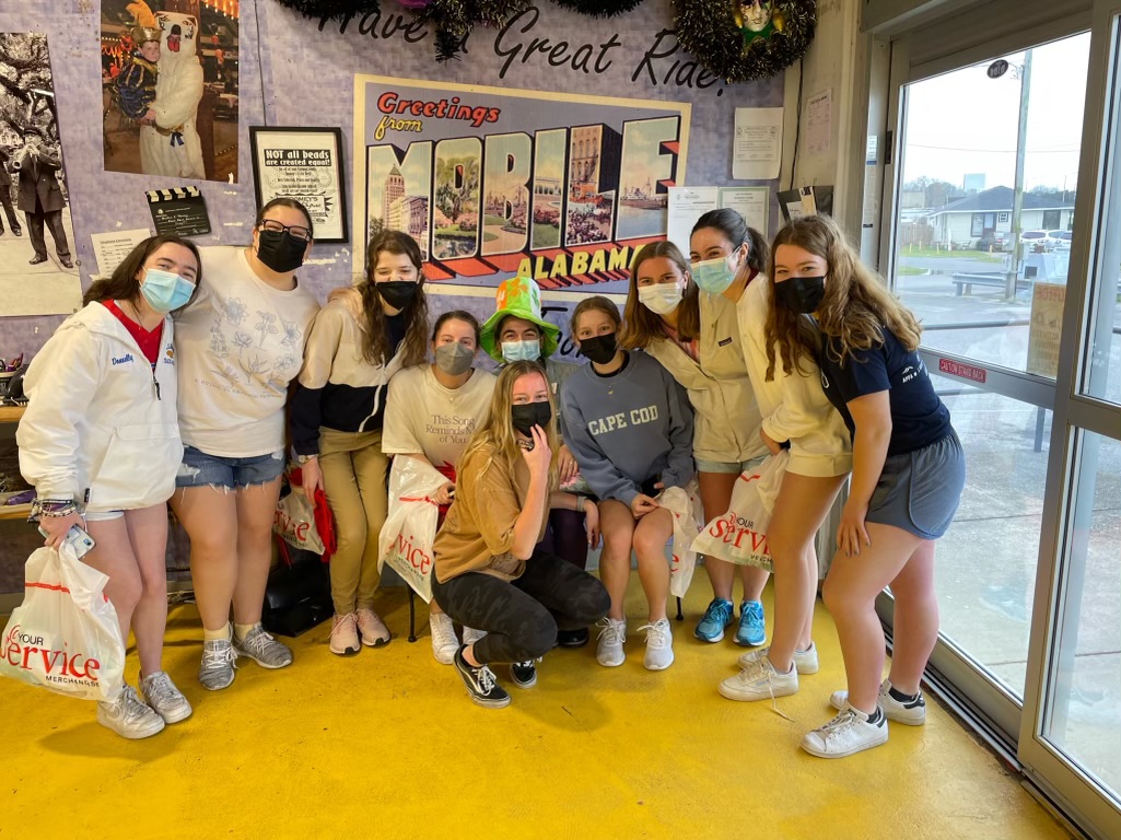 A group of students huddled in front of a sign that reads &quot;Greetings from Mobile&quot;