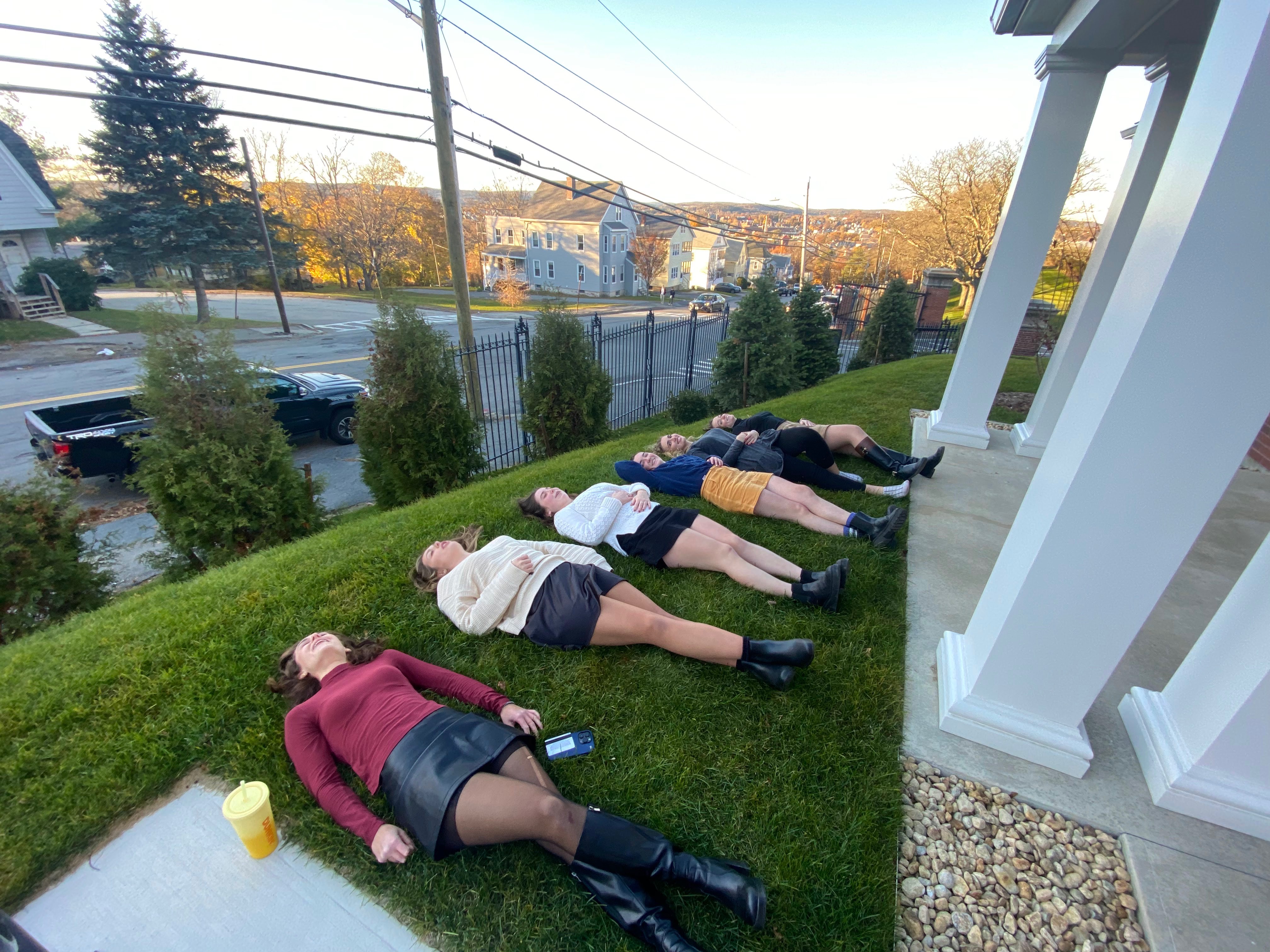 Several young women lying down in grass with the sun setting in the background