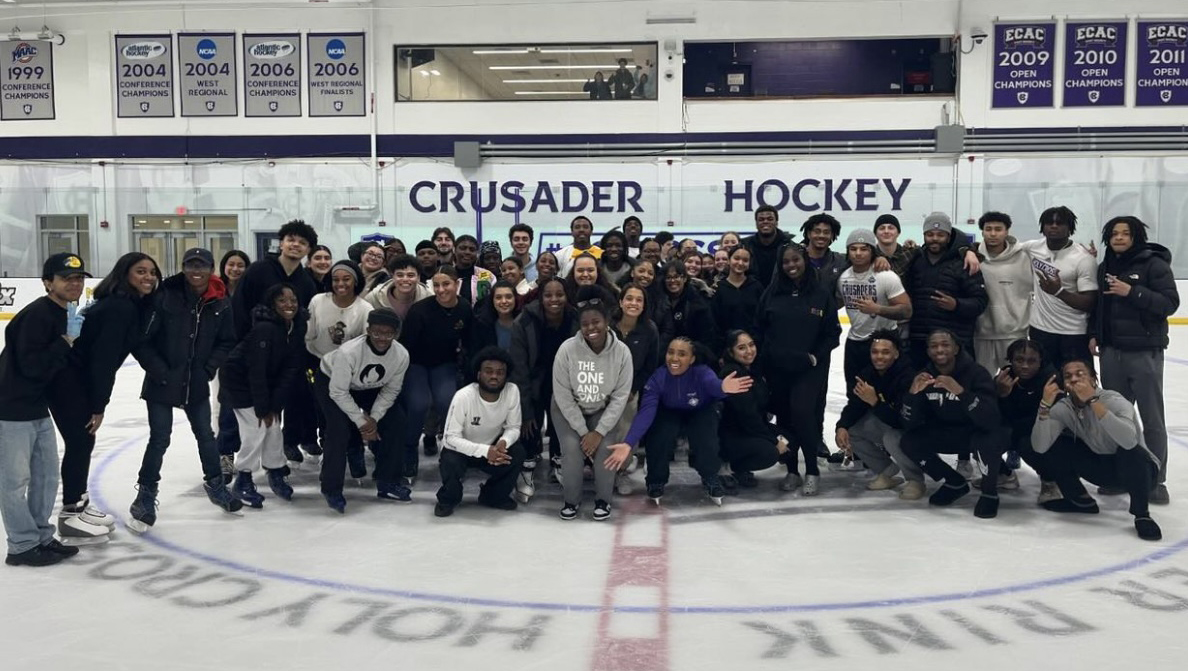 A group of students huddle together smiling inside the Holy Cross ice rink.