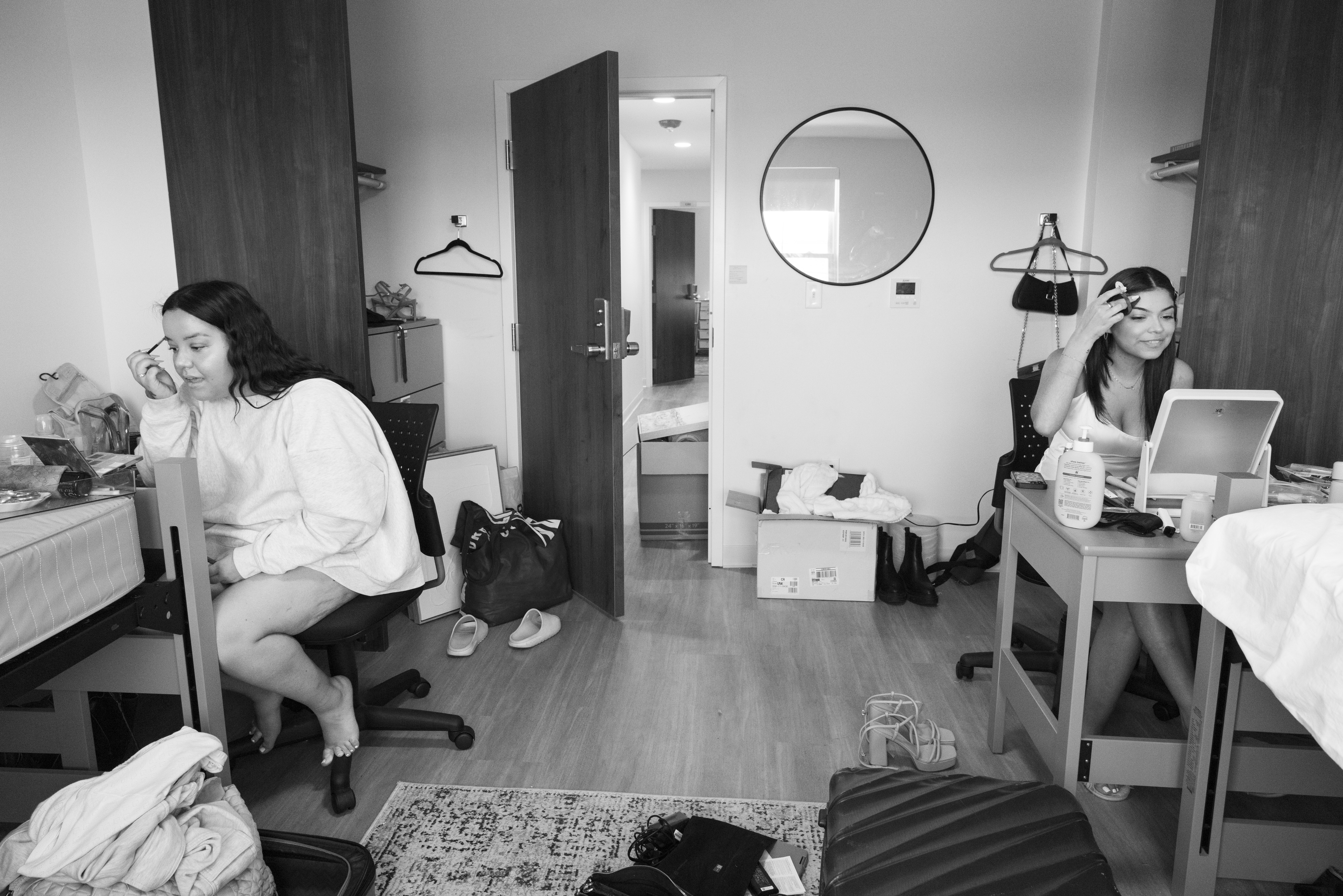 Roommates sit on opposite sides of the room applying makeup in small mirros