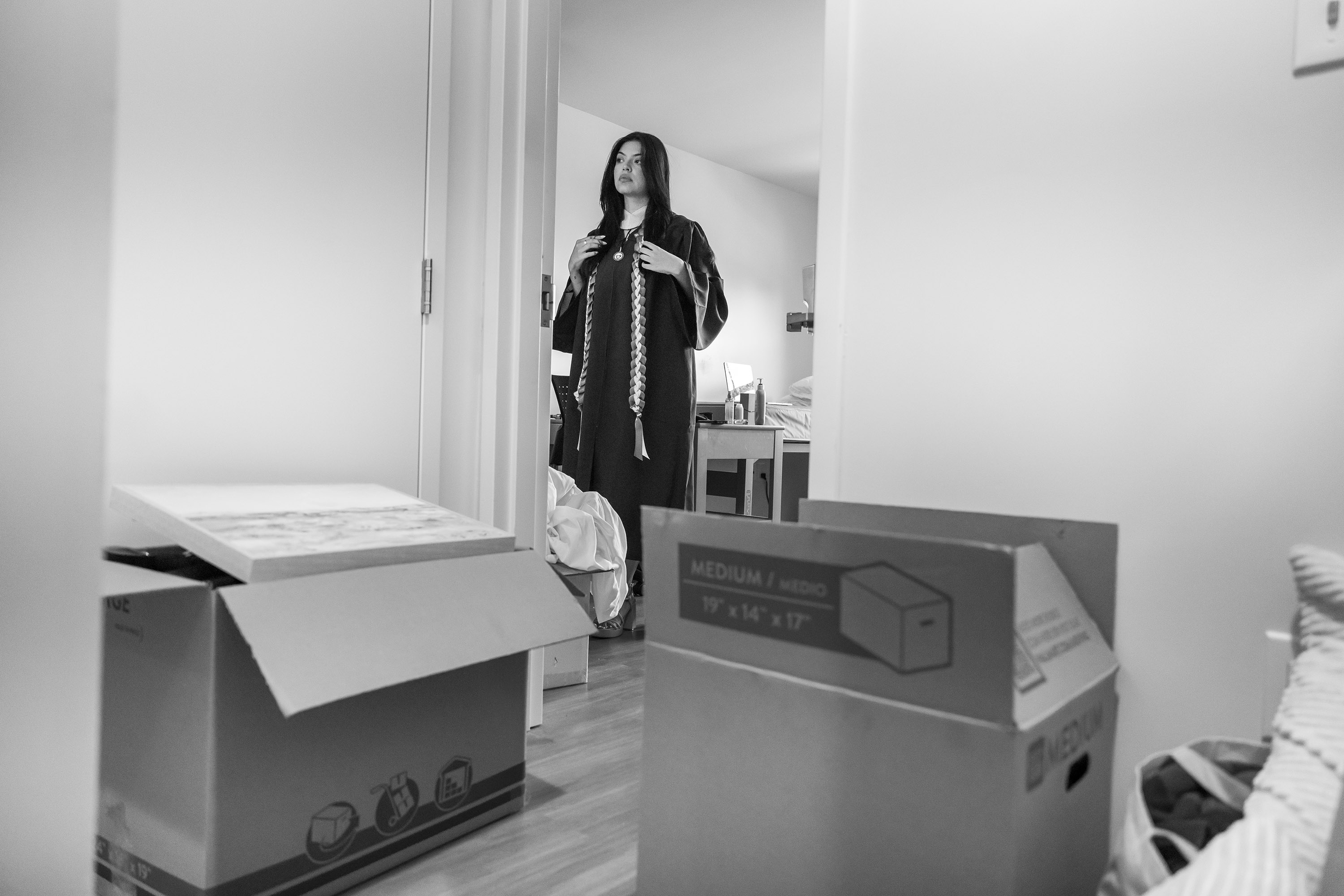 A woman adjusts her gown in the mirror with boxes in the foreground.