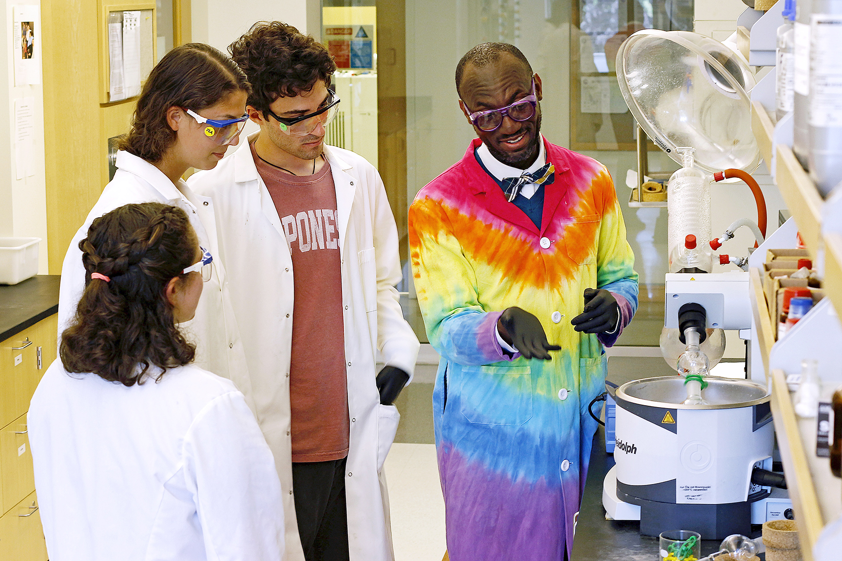 A man in a tie-dyed lab coat with college students in a lab