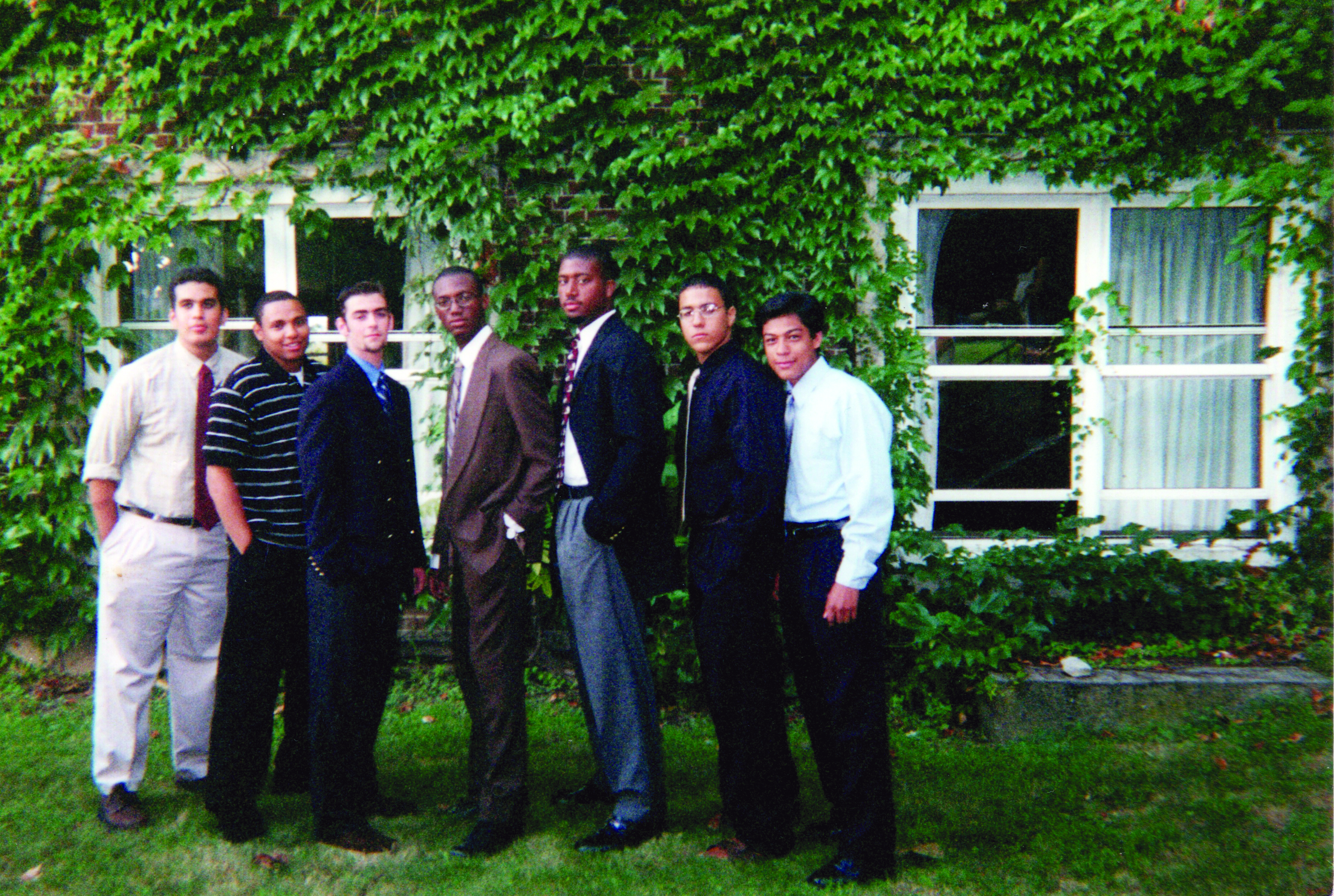 A group of men standing in front of an ivy-covered wall