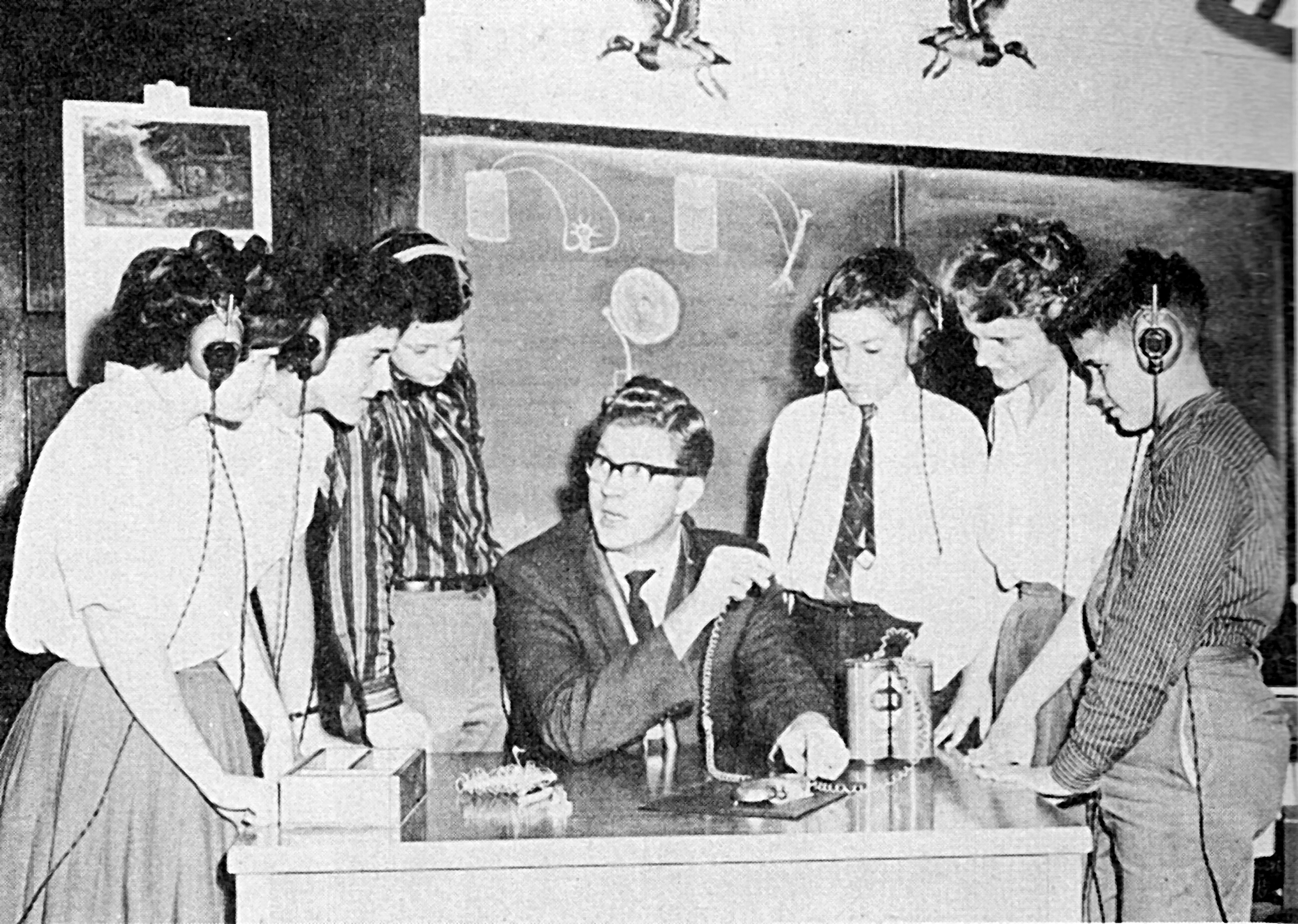 Black and white photo of students standing around a teacher