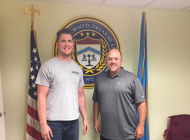 Two people stand in front of a sign for the Bureau of Alcohol, Tobacco, Firearms, & Explosives