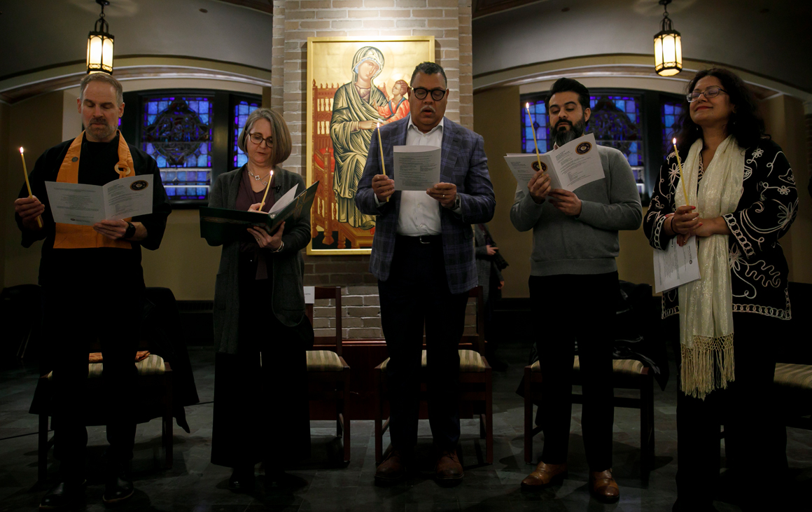 Five people stand shoulder to shoulder singing