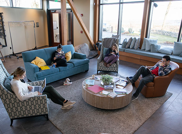 Four students sit in chairs with books and computers