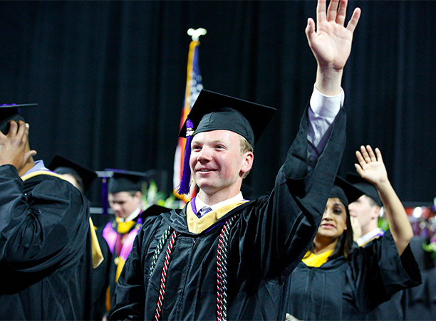 A student waves while processing into the DCU Center.