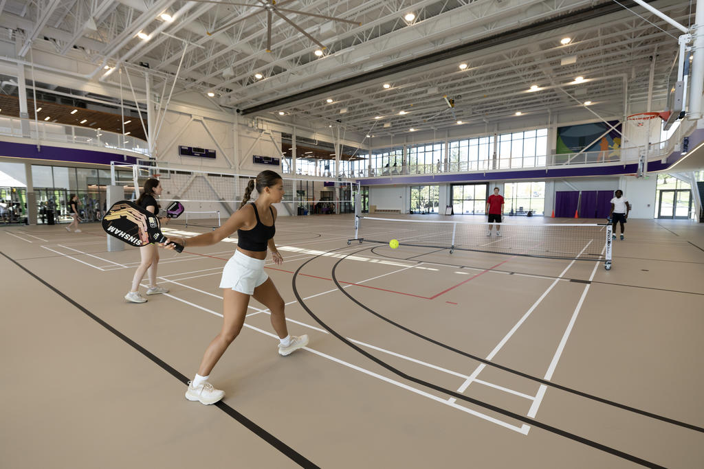 A student hits the ball in a pickleball match indoors