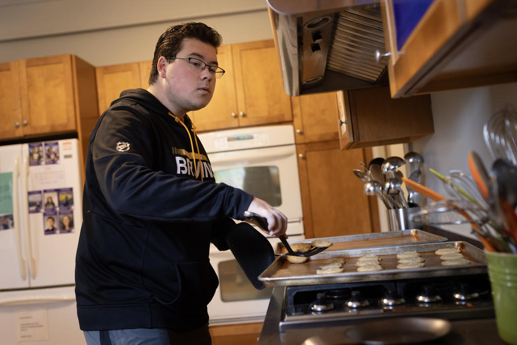 Man takes cookies off a sheet pan with a spatula