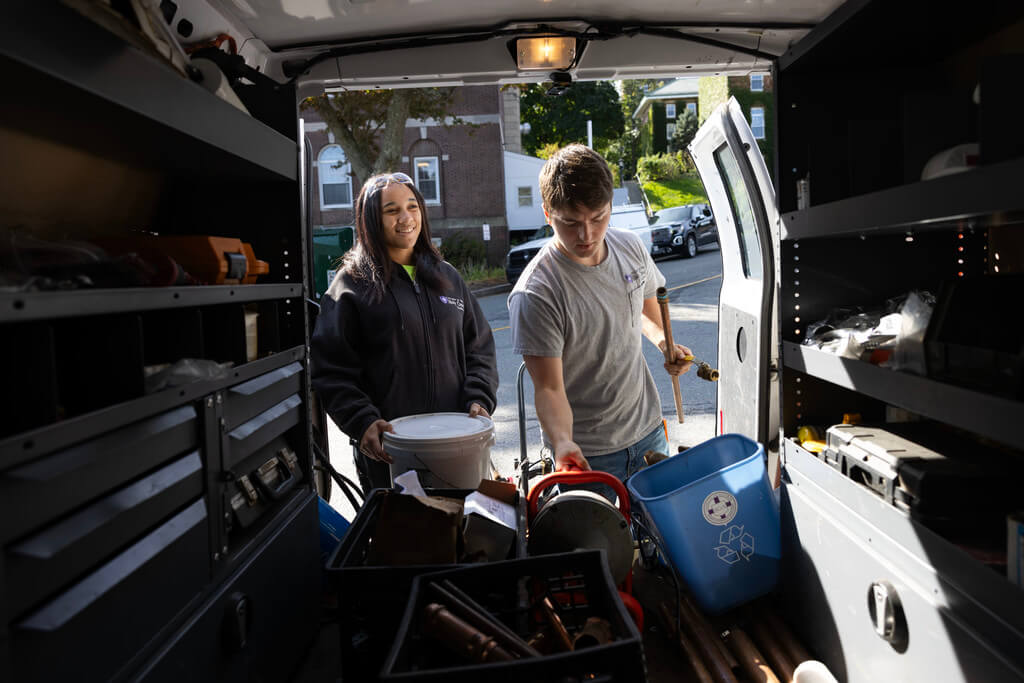 Two people reach for equipment in the back of a van