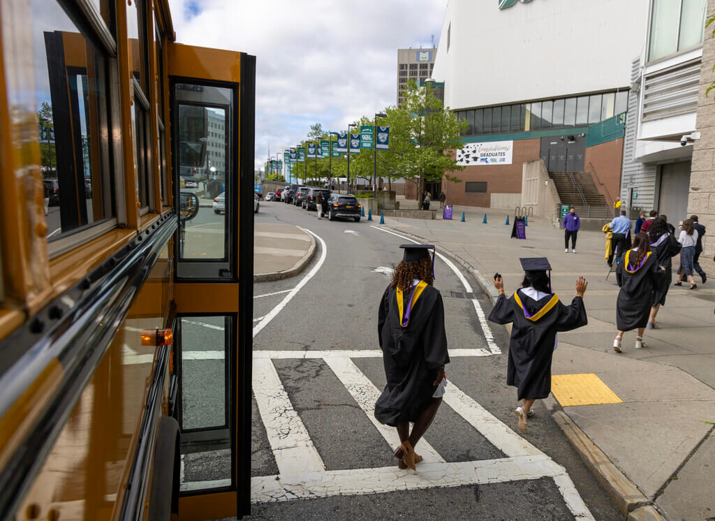 Students in graduation robes disembarking from a school bus