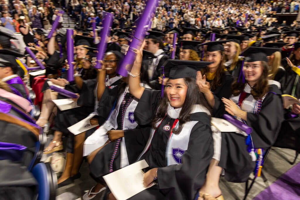 Seated students holding diplomas and cheering