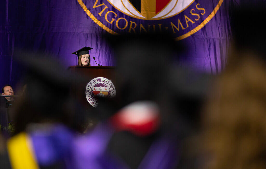Female student in cap and gown addresses audience at commencement ceremony