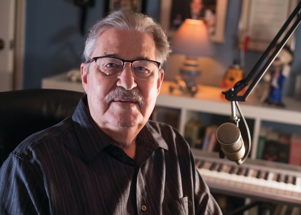 Man in glasses sits at microphone
