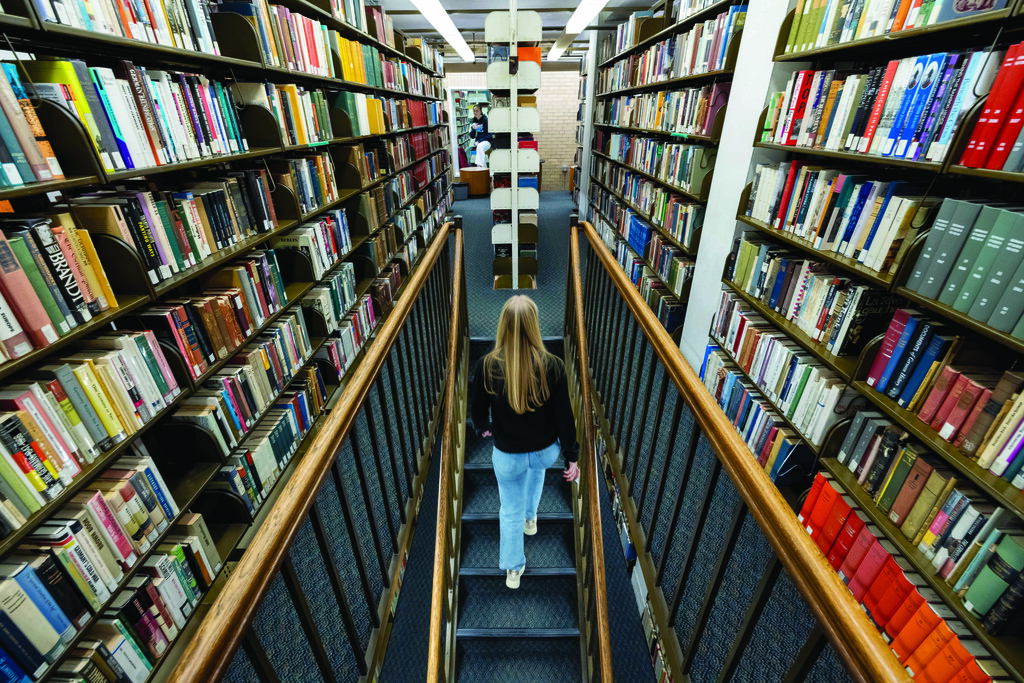 Student walking up stairs amongst library shelves