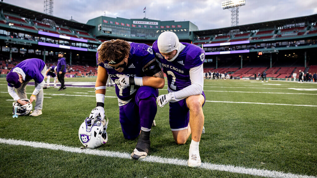 Two Holy Cross football players kneeling on the field