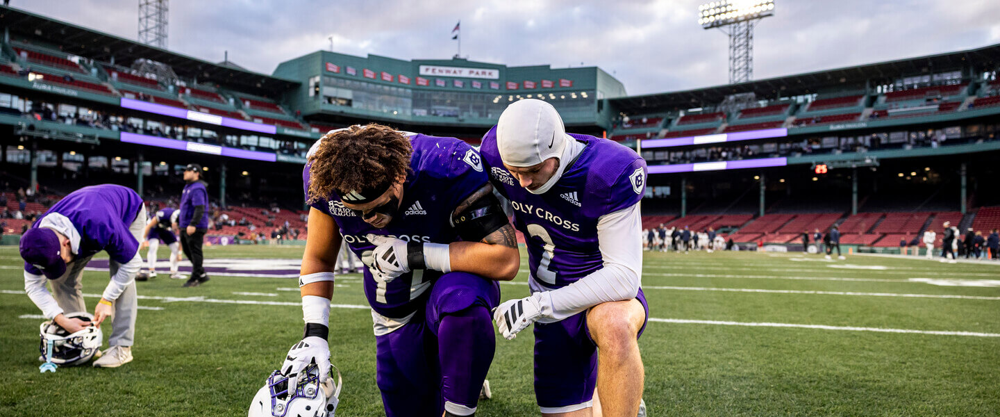 Two Holy Cross football players kneeling on the field