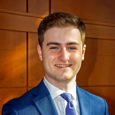 Young man in suit with wood paneled background.
