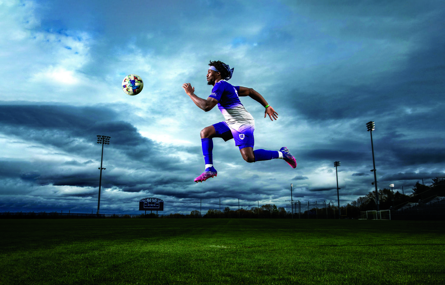 A soccer player in a purple uniform jumping in the air for a soccer ball that is at eye level