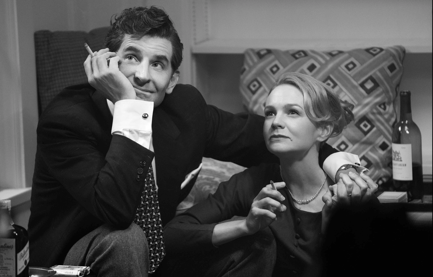 Man with a cigarette in one hand rests his arm across the shoulders of a woman