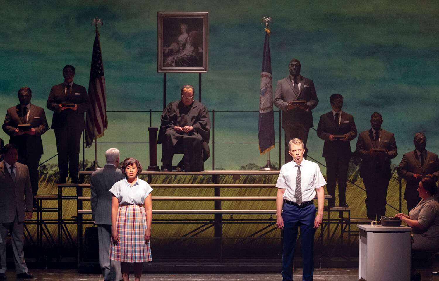 Man and woman standing on stage with members of the chorus on bleachers