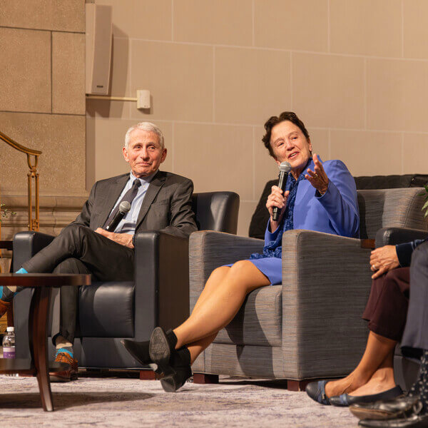 Seated woman speaks into microphone flanked by three other seated people