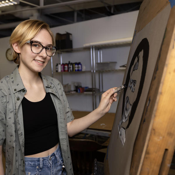 Young artist poses in front of drawing easel.