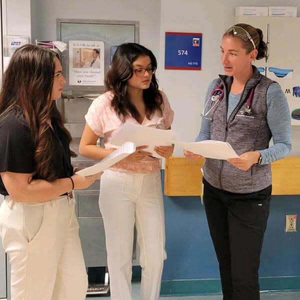 Three women discussing medical charts in clinical setting.