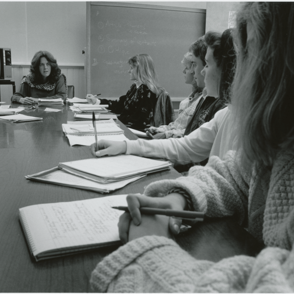 Female professor sitting at table with six female students.