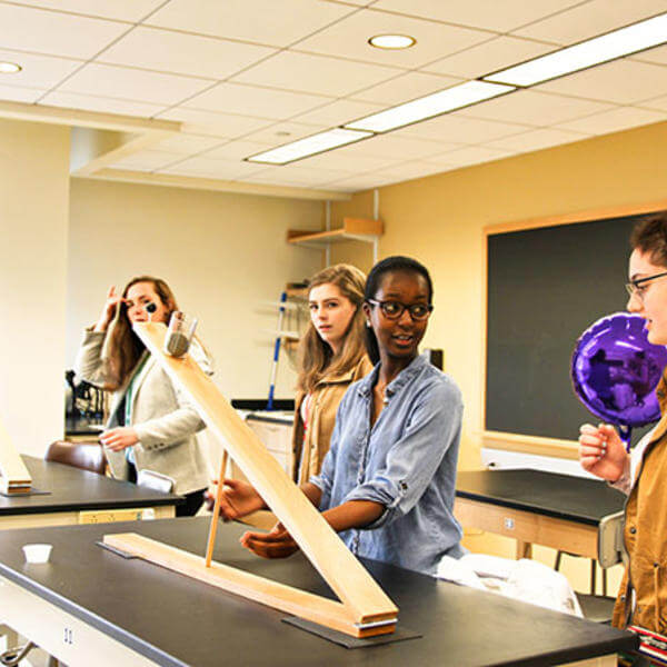 Students stand around a table with large pieces of wood
