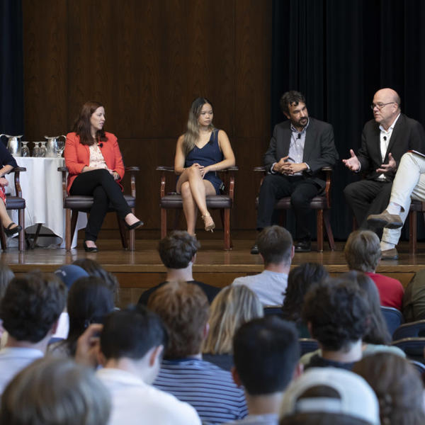 Group of people sit on stage as part of a symposium discussion.