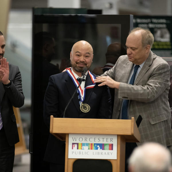 Man stands a podium with honorary medal around his neck