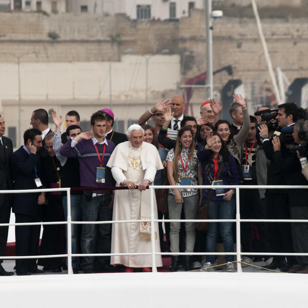 Pope Benedict XVI stands with a crowd on a dock.